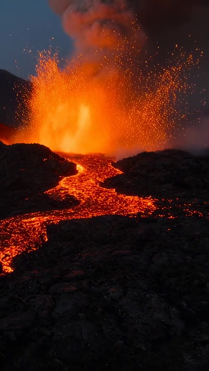 Video verticale: Sfiato incandescente che erutta lava e scintille, un fiume di lava che avanza su un campo di lava scuro.