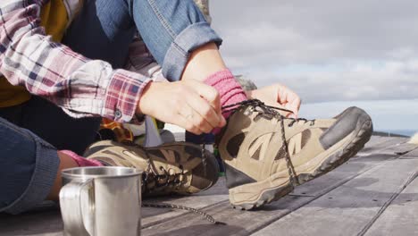 low section of caucasian woman camping, sitting outside tent putting on boots in rural setting