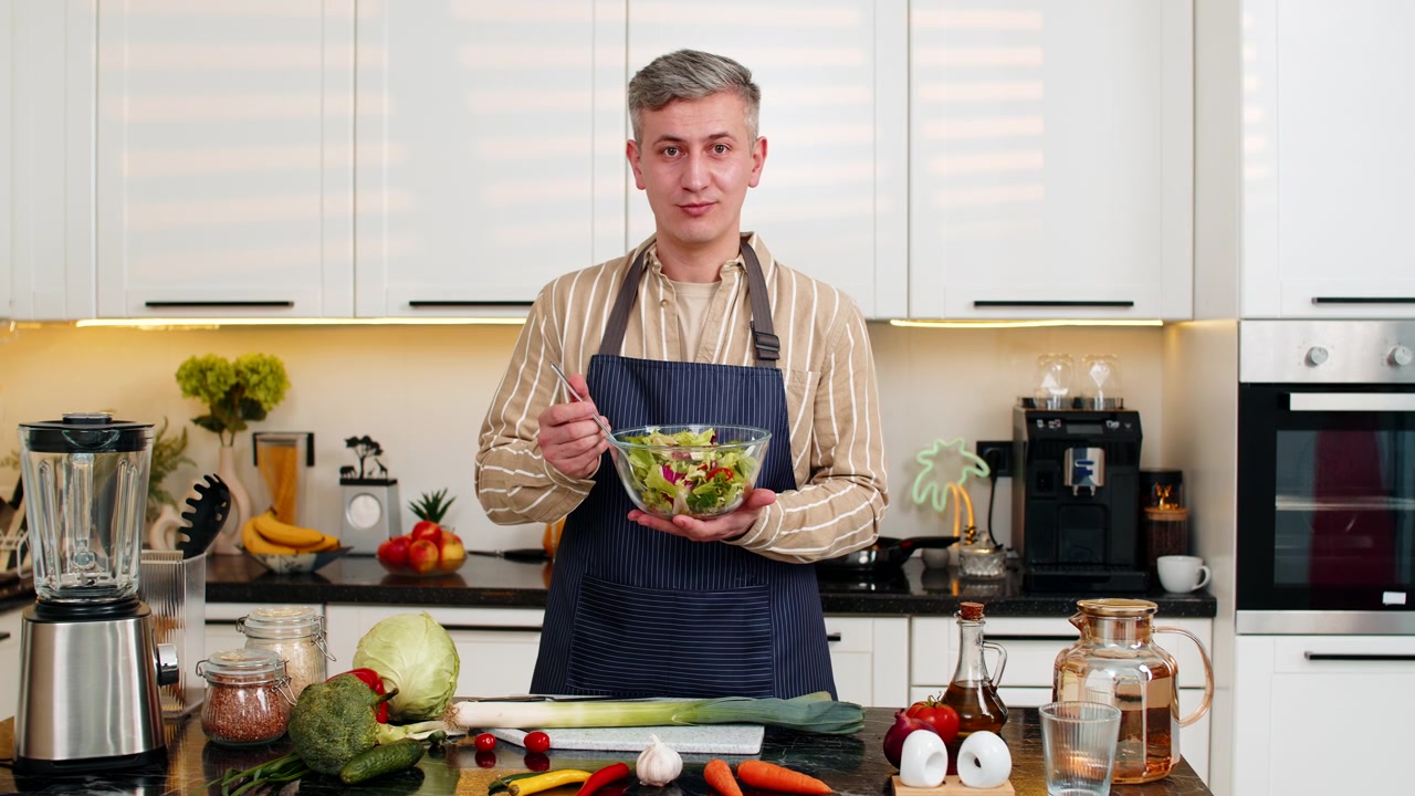 Mann mittleren Alters hält frischen Gemüsesalat in der Küche und teilt Ernährungstipps für gesunde Ernährung.