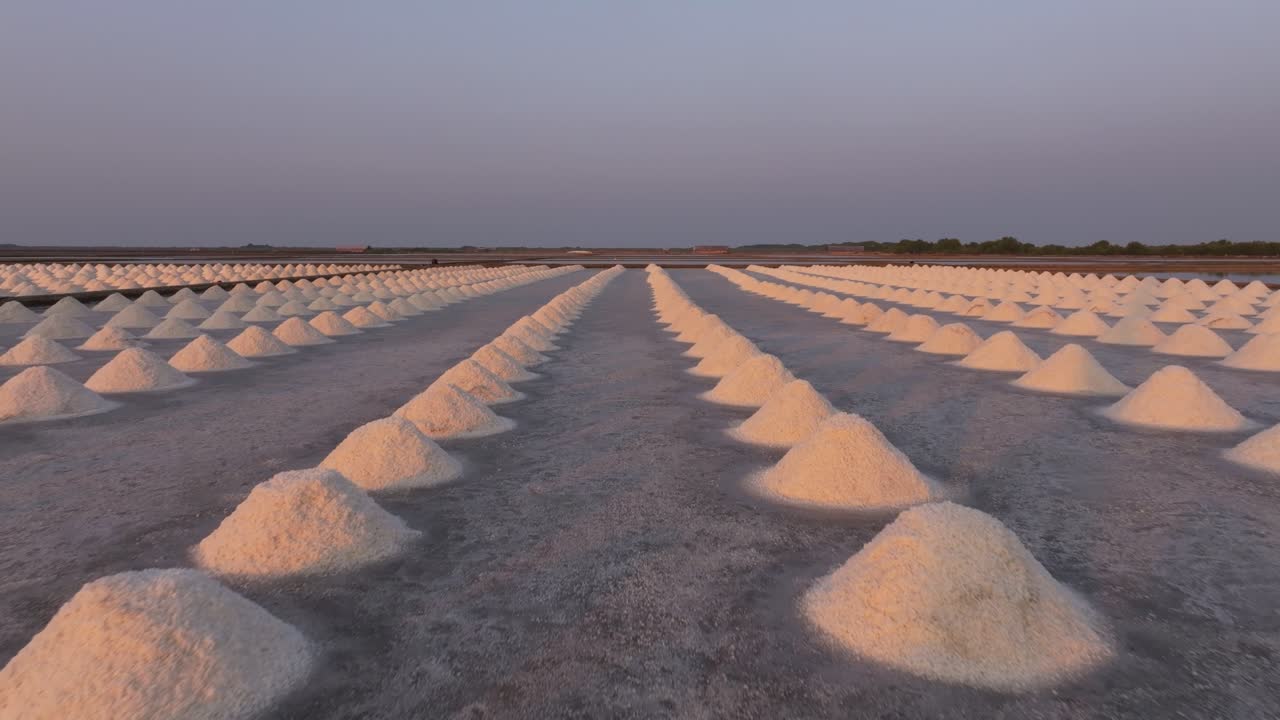 Droneoptagelse af en saltfarm med bunker af råsalt ved solnedgang, Petchaburi, Thailand.