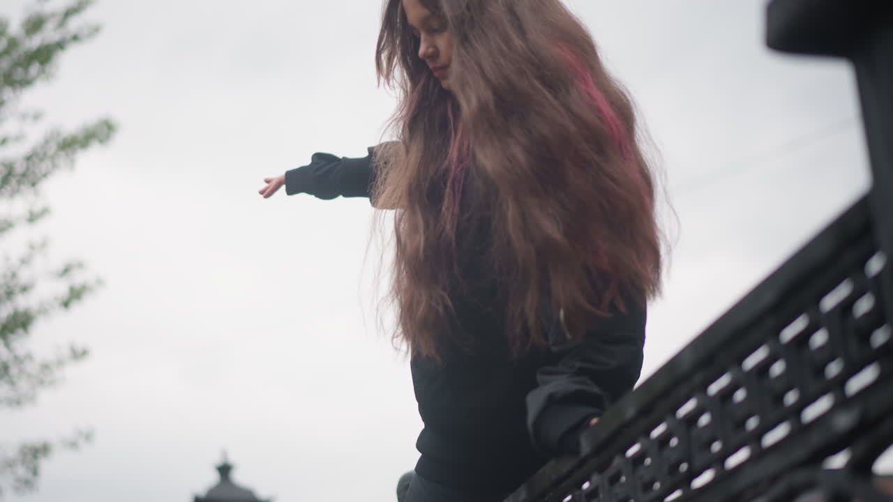 Regnerische Stadtbrücke mit selbstbewusster Frau, die geht. Frau mit gefärbtem rosa Haar überquert nachts eine regnerische Stadtbrücke. Stadtszene mit einer Frau mit rosa Haar, die nachts über eine nasse Brücke geht.