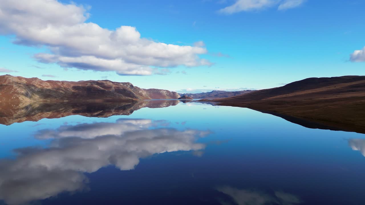 Blue sky clouds reflect in mirror lake surface in summer arctic tundra