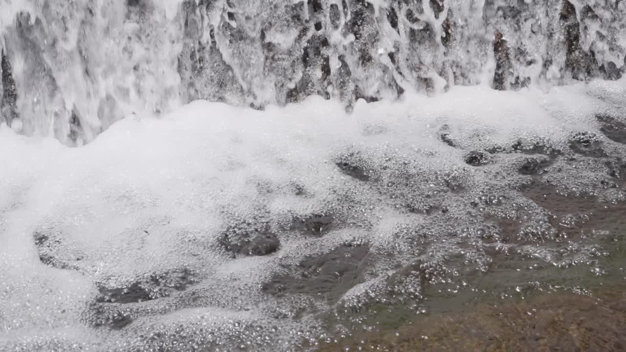 Close-up of white foamy water swirling at the base of a waterfall in a natural setting