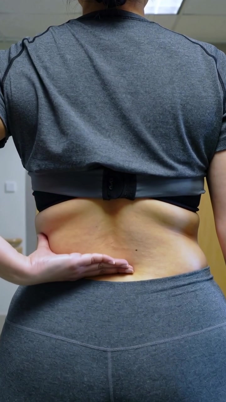 Video verticale: Donna che solleva un top corto, massaggiando la zona lombare per alleviare il dolore, con la fascia del reggiseno visibile