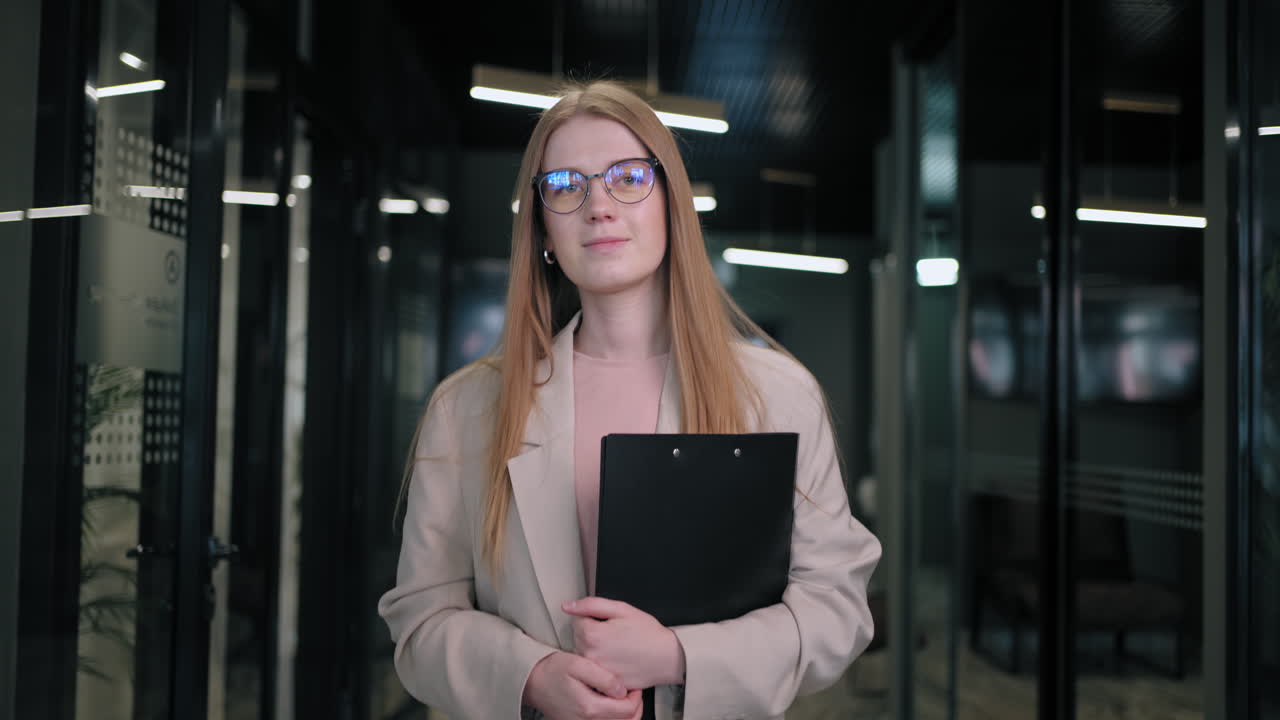 Portrait of a business woman with glasses walking down the corridor of a business center with papers