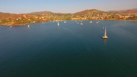 tilting up to reveal a busy ocean bay in zihuatanejo, mexico at sunset as the sailboat and yachts return to anchor near shore