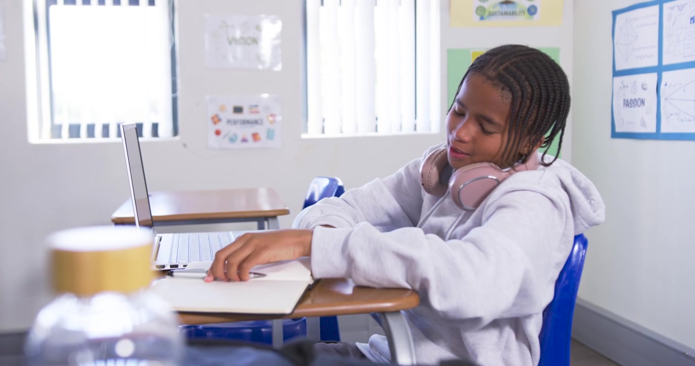 Adolescente afroamericana che si unisce alla lezione alla scrivania, indossa una cuffia, usa un laptop e prende appunti, con spazio per il testo.