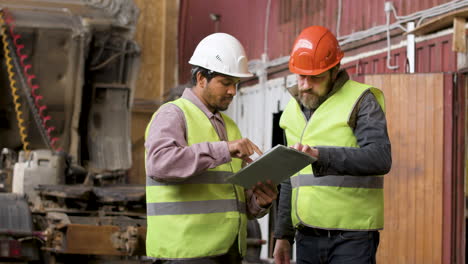 Boss-And-Worker-Wearing-Vests-And-Safety-Helmets-Organizing-A-Truck-Fleet-In-A-Logistics-Park-While-They-Consulting-A-Document-6