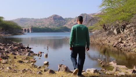 isolated-young-man-walking-and-sitting-at-stone-at-pristine-lake-shore-at-morning