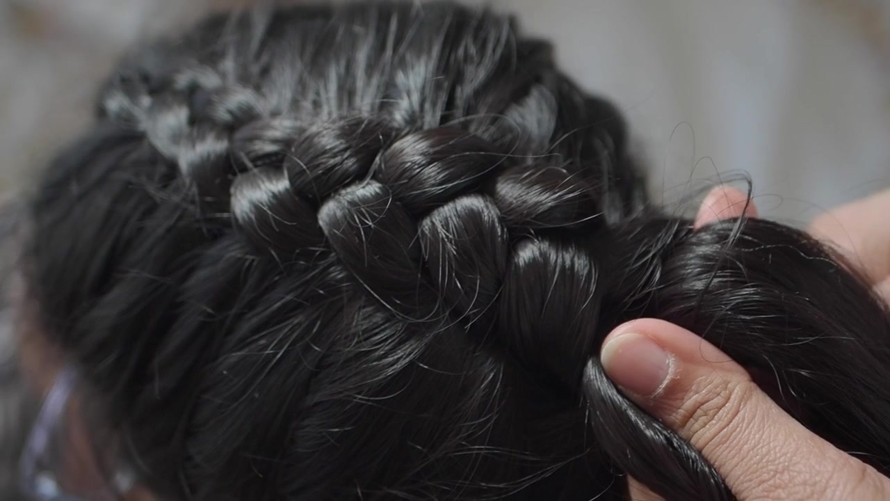 Stilista che intreccia lunghi capelli scuri in un salone
