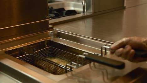 Preparing-French-fries-in-metal-mesh-basket-submerged-into-hot-boiling-vegetable-oil