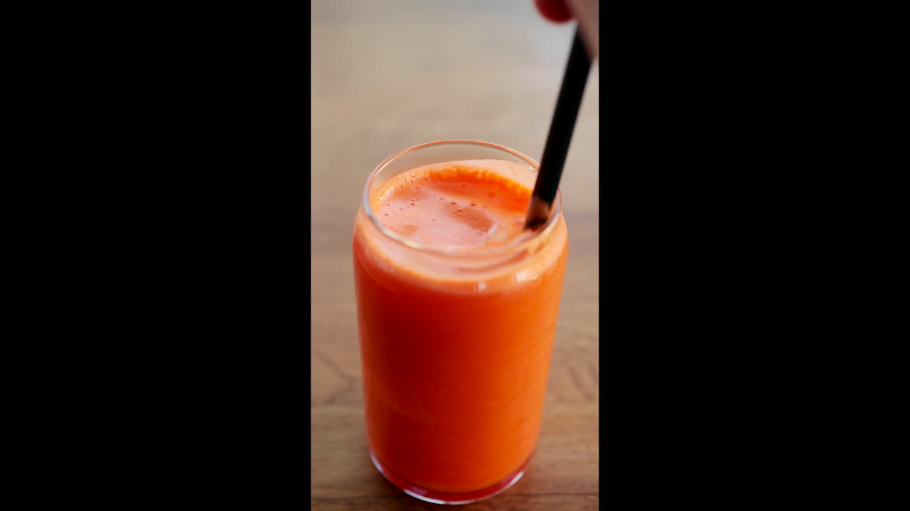 Succo d'arancia fresco mescolato in un bicchiere con una cannuccia, che crea schiuma e bollicine