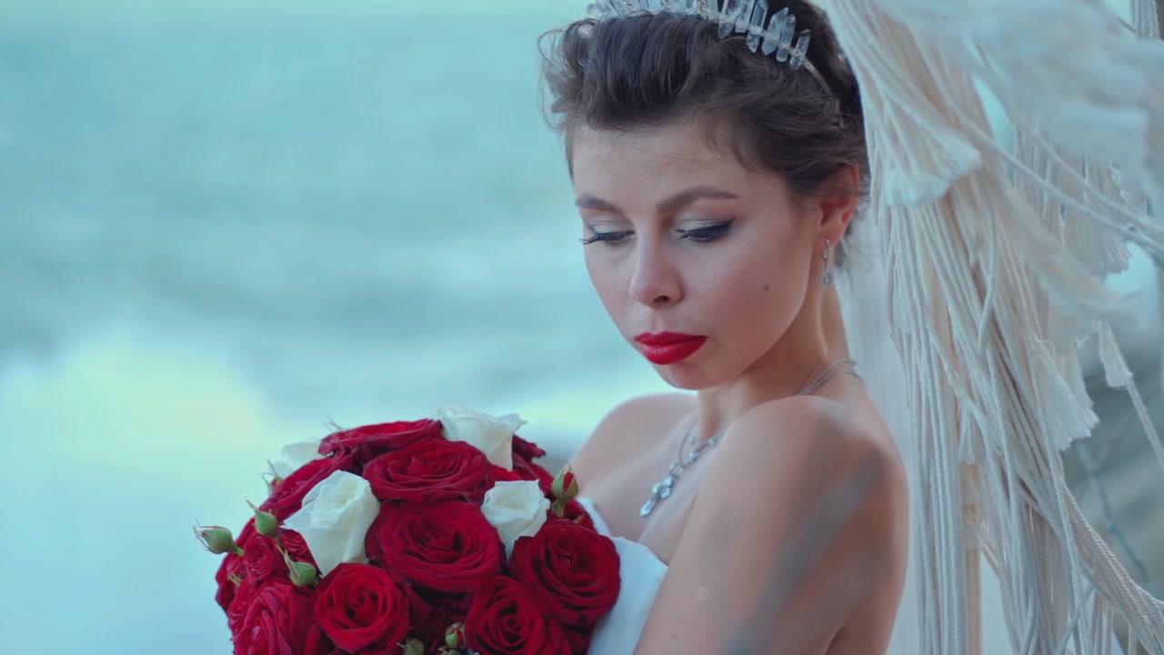 Bella Sposa che Tiene un Bouquet di Rose Rosse e Bianche Vicino all'Oceano