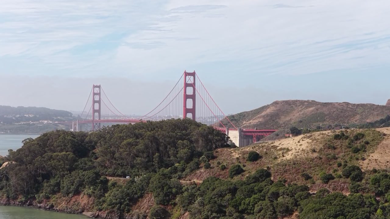 Vista panoramica del famoso Golden Gate Bridge a San Francisco, California, incorniciato dalle lussureggianti colline verdi delle Marin Headlands sotto un cielo parzialmente nuvoloso durante una giornata velata. Vista ascendente da drone.