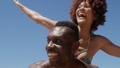 Shirtless-man-giving-piggyback-ride-to-woman-at-beach-4k