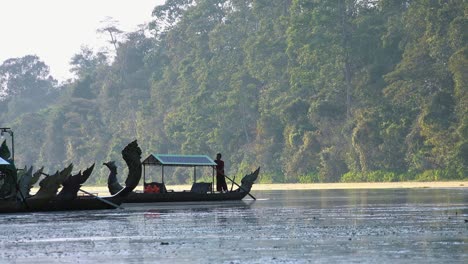 amplia toma exterior de un remero girando el bote del dragón en un río con un exuberante fondo costero