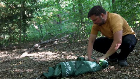 Close-up-slow-motion-of-man-tourist-rolling-up-a-tent-at-forest-campsite-and-packing-up-to-leave