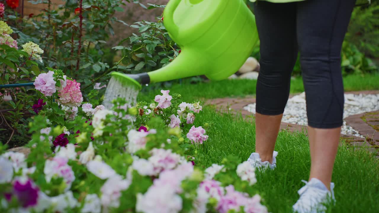 Mulher regando flores coloridas em um jardim verde exuberante.