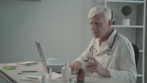 a grey haired, middle aged doctor consults on his laptop the composition of a medicine 2