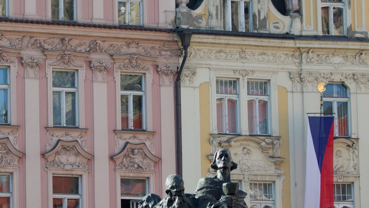 Daytime camera pan reveals Jan Hus Memorial, baroque architecture, Czech flags, and city square