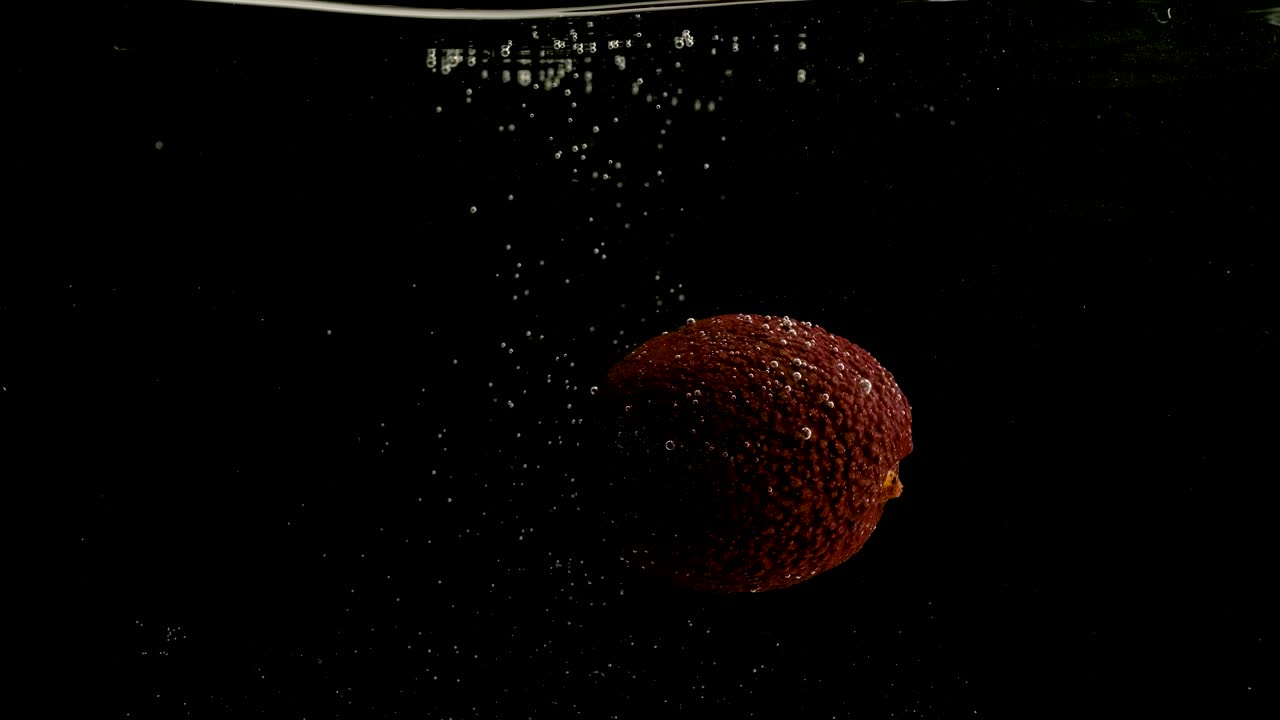 el aguacate cayendo en el agua sobre un fondo negro. brillante video de alta calidad