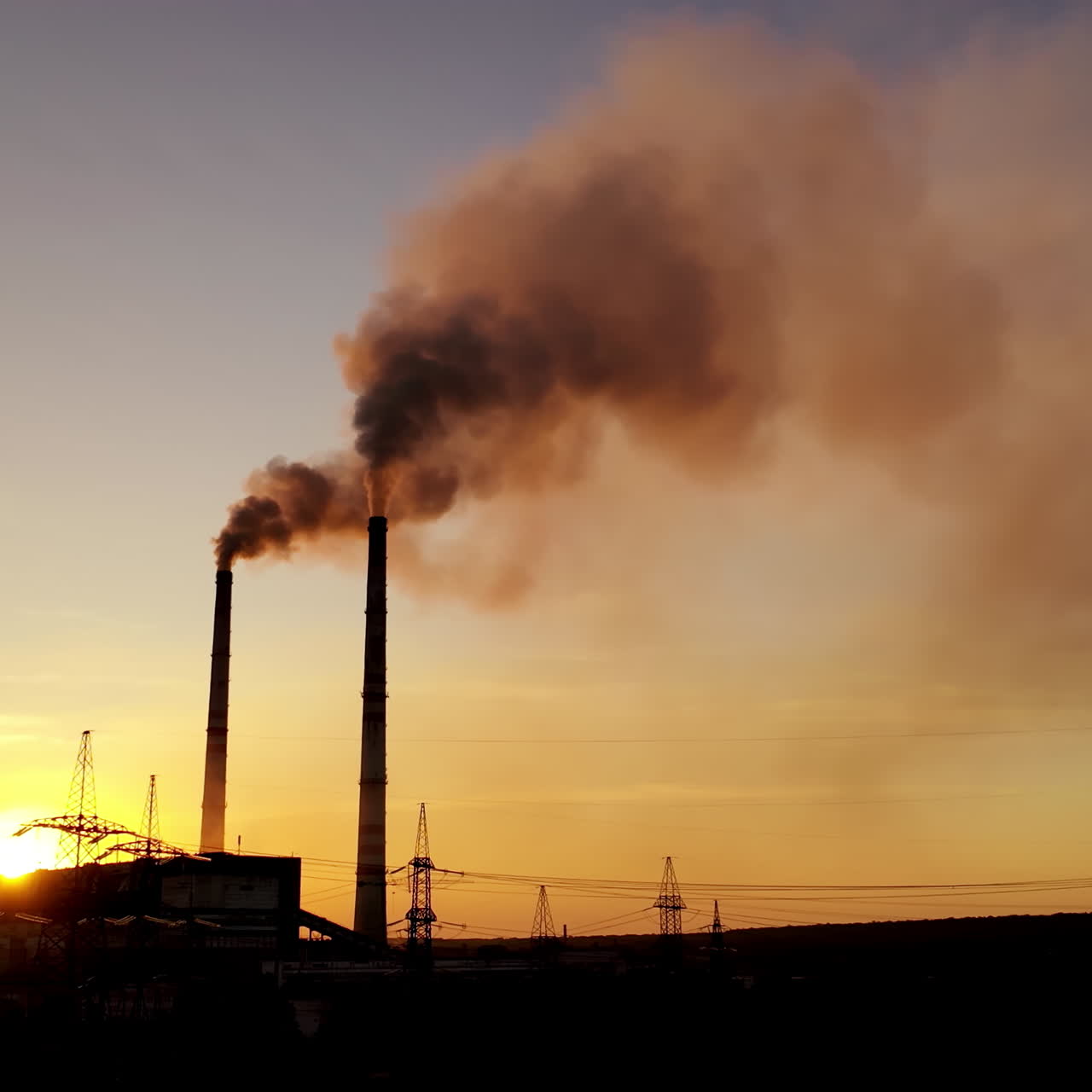 Evening background of industrial factory. Dirty smoke goes from pipes at sunset. Metallurgical plant with smoke on the evening sky.