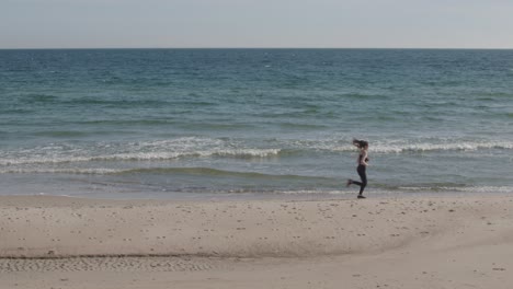 young fitness female jogging on beach with green ocean blue sky horizon bright sand