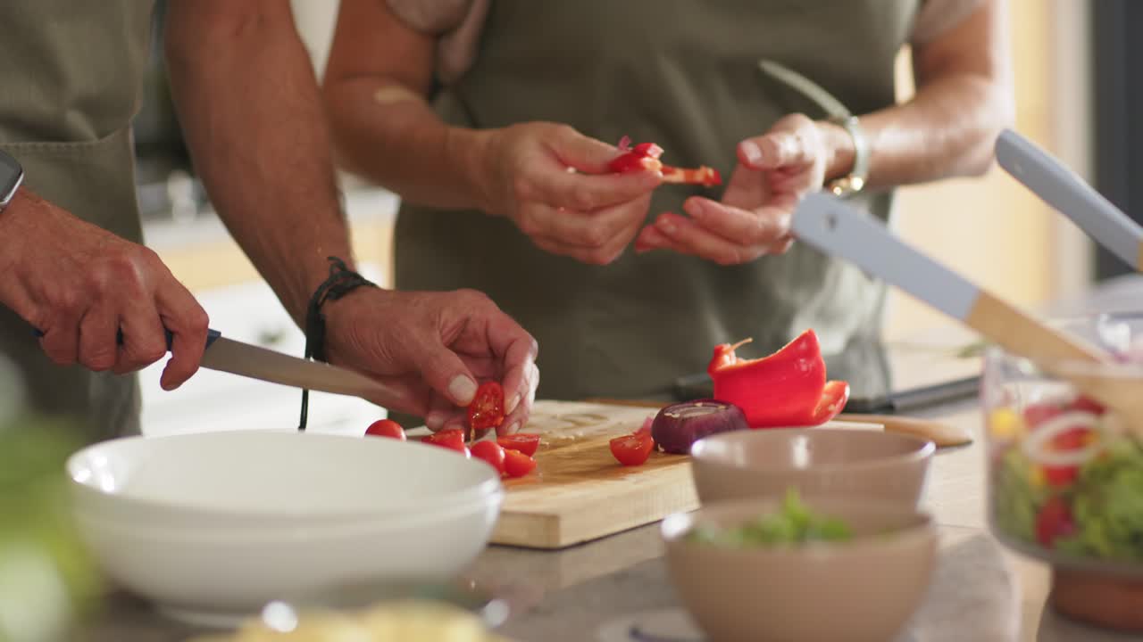 Diverse couple reaching red pepper, chopping on board, placing cores in canister for salad