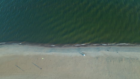 Aerial-view-from-above-person-flying-kite-sail-on-calm-sunny-beach-birds-eye-view