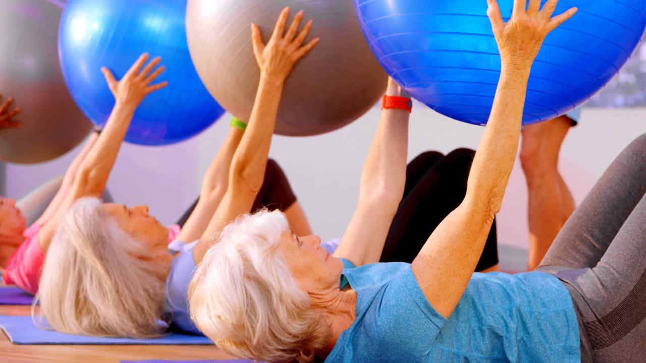 Trainer assisting senior woman in performing yoga 4k