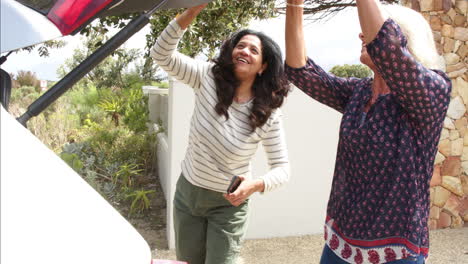 two happy diverse senior women closing car trunk and giving high five on sunny day, slow motion