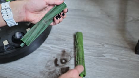 woman removing tangled hair from robotic vacuum rollers, close-up view.