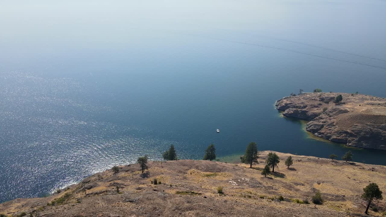 Small boat anchored near the dry and rocky shore of Okanagan Lake during wildfire season