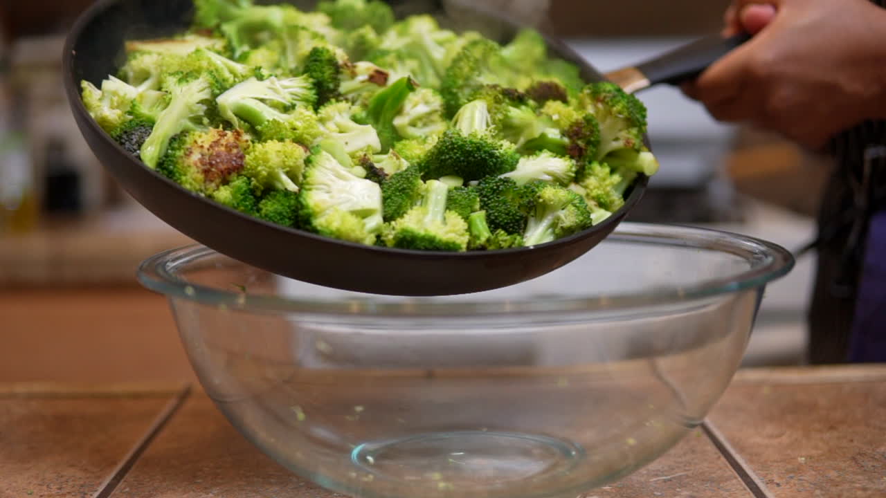 갓 익힌 브로콜리로 가득 찬 팬을 유리 그릇에 조심스럽게 흔드는 것 - 슬로우 모션