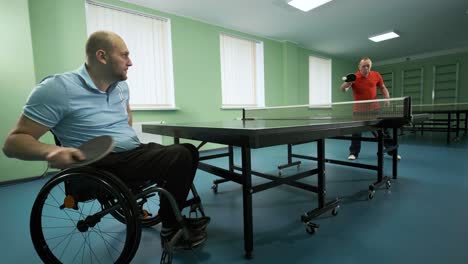 a man in a wheelchair plays ping pong. people with disabilities play table tennis. rehabilitation of the disabled. paralympic sport.