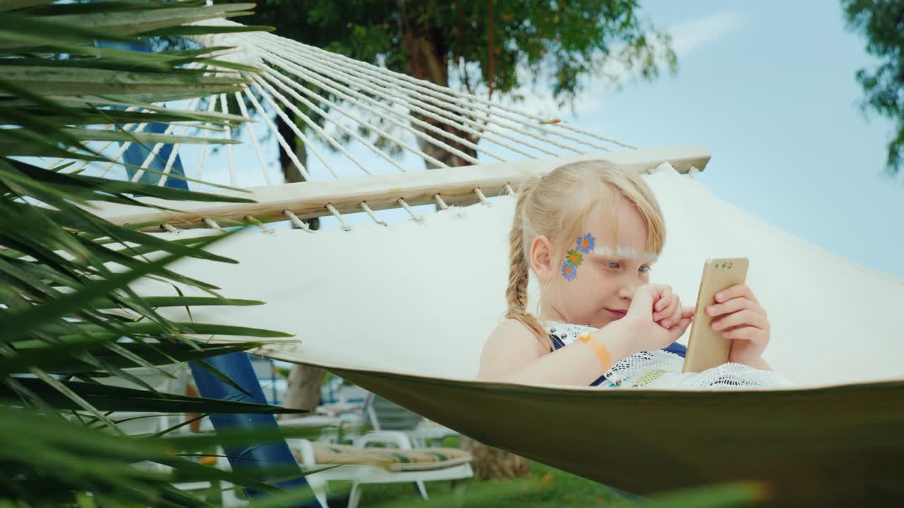 una chica genial con agua sucia juega en el teléfono en una hamaca en un hotel turístico