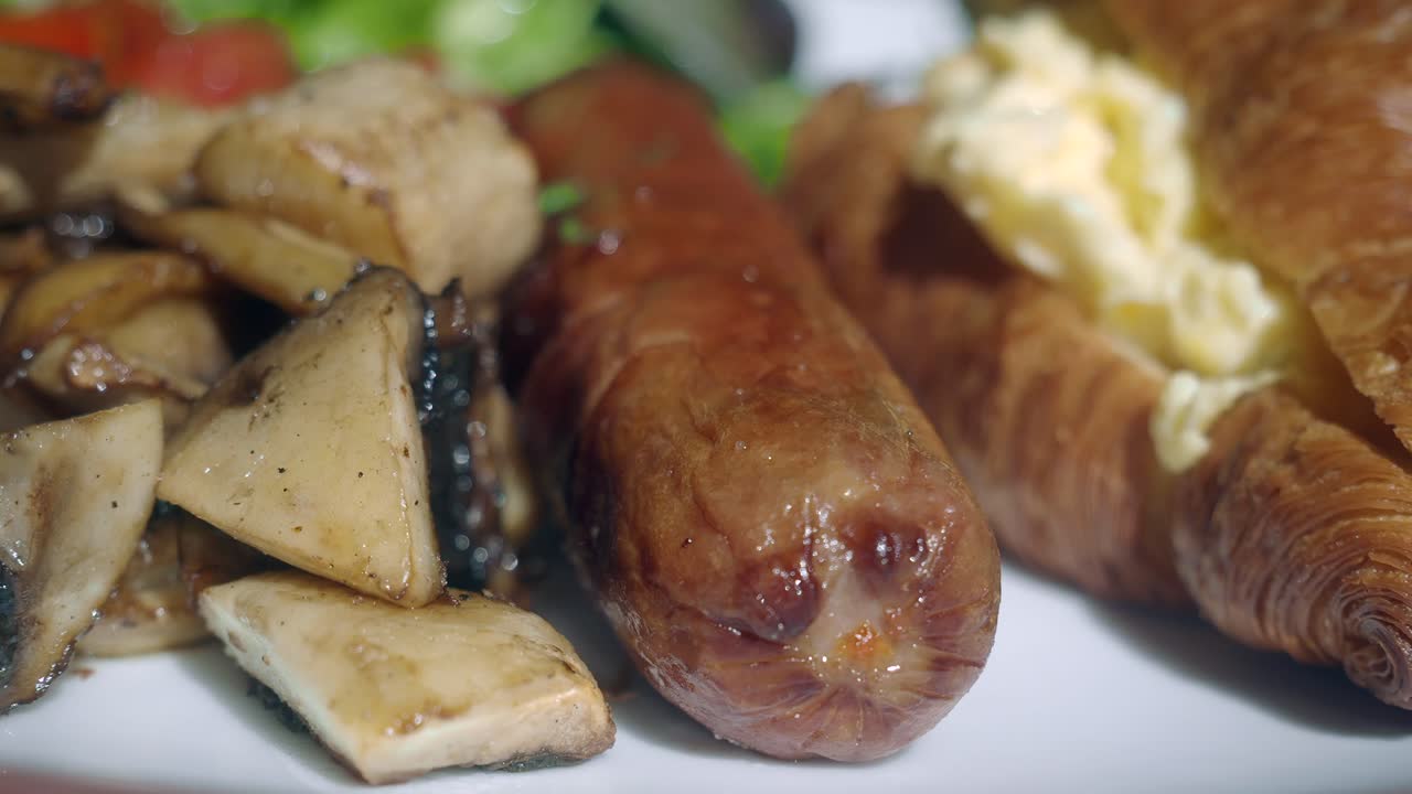 Close-up of a breakfast plate with sausage, mushrooms, and a croissant with scrambled eggs