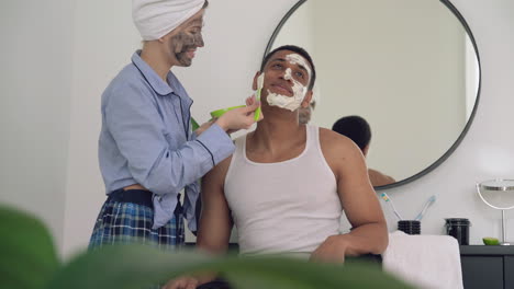 woman with facial mask applying scrub to a handsome black man