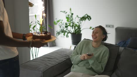 a husband brought the birthday cake with big sparkling candle to his wife in the living room