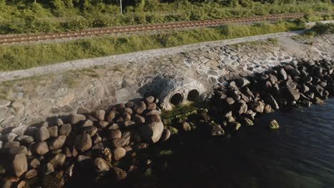 drone shot of sunlight beaming on a drain pipes surrounded by rocks