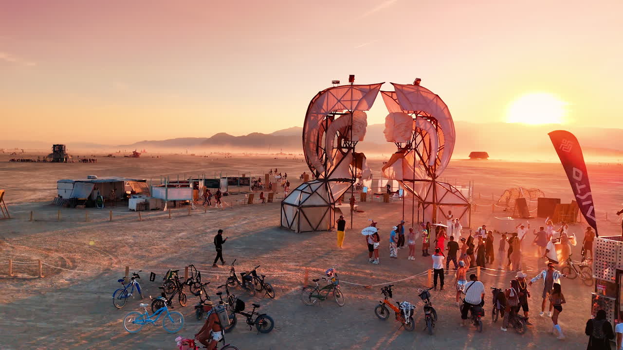 Nevada, USA, 25 August 2025: Drone view of people gathering near a large art installation at Burning Man during sunrise with desert mountains in the background