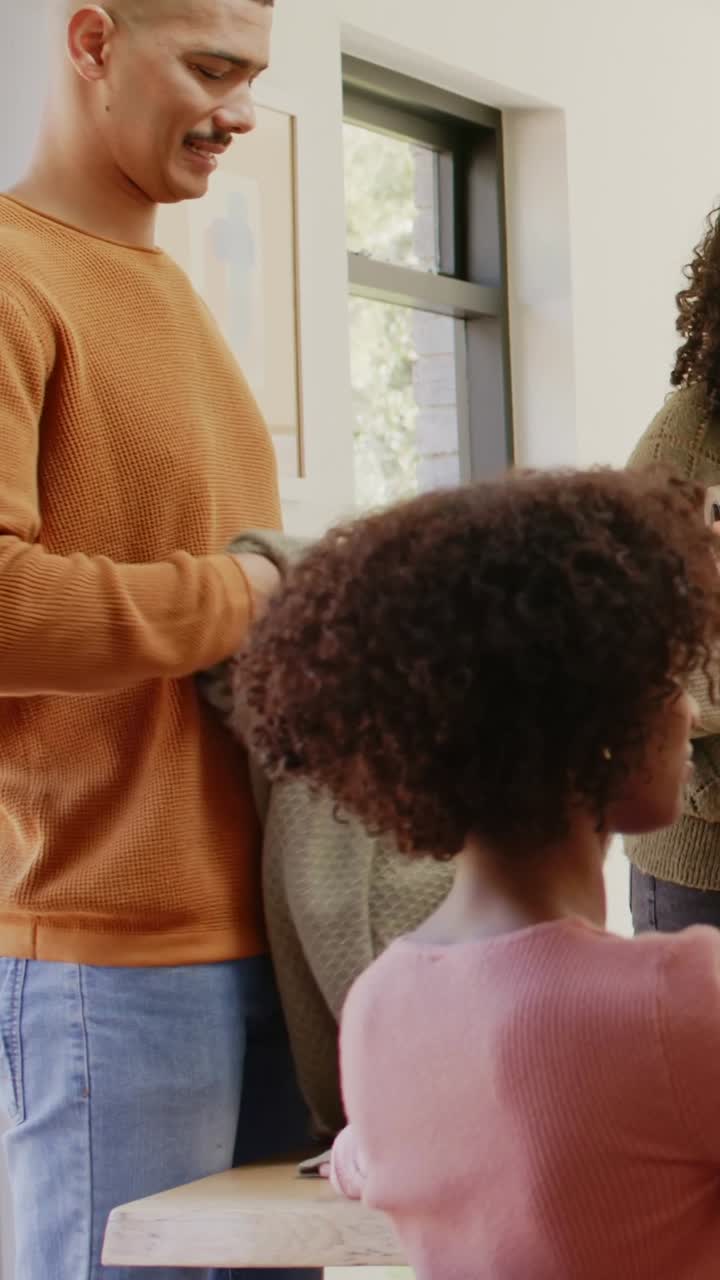 Video verticale: Una donna con un maglione color oliva sistema dei capi in maglia su un tavolo mentre un uomo arriva con un capo in maglia grigio.