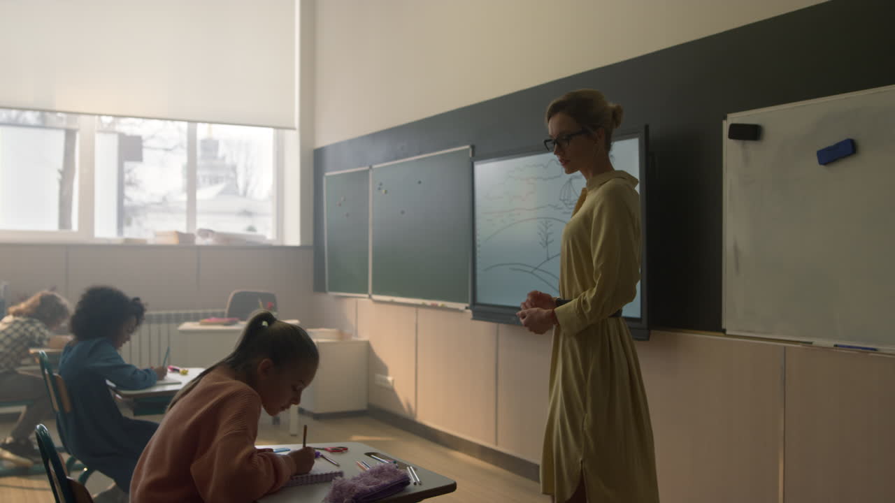 Female teacher standing at blackboard in front of class full of children
