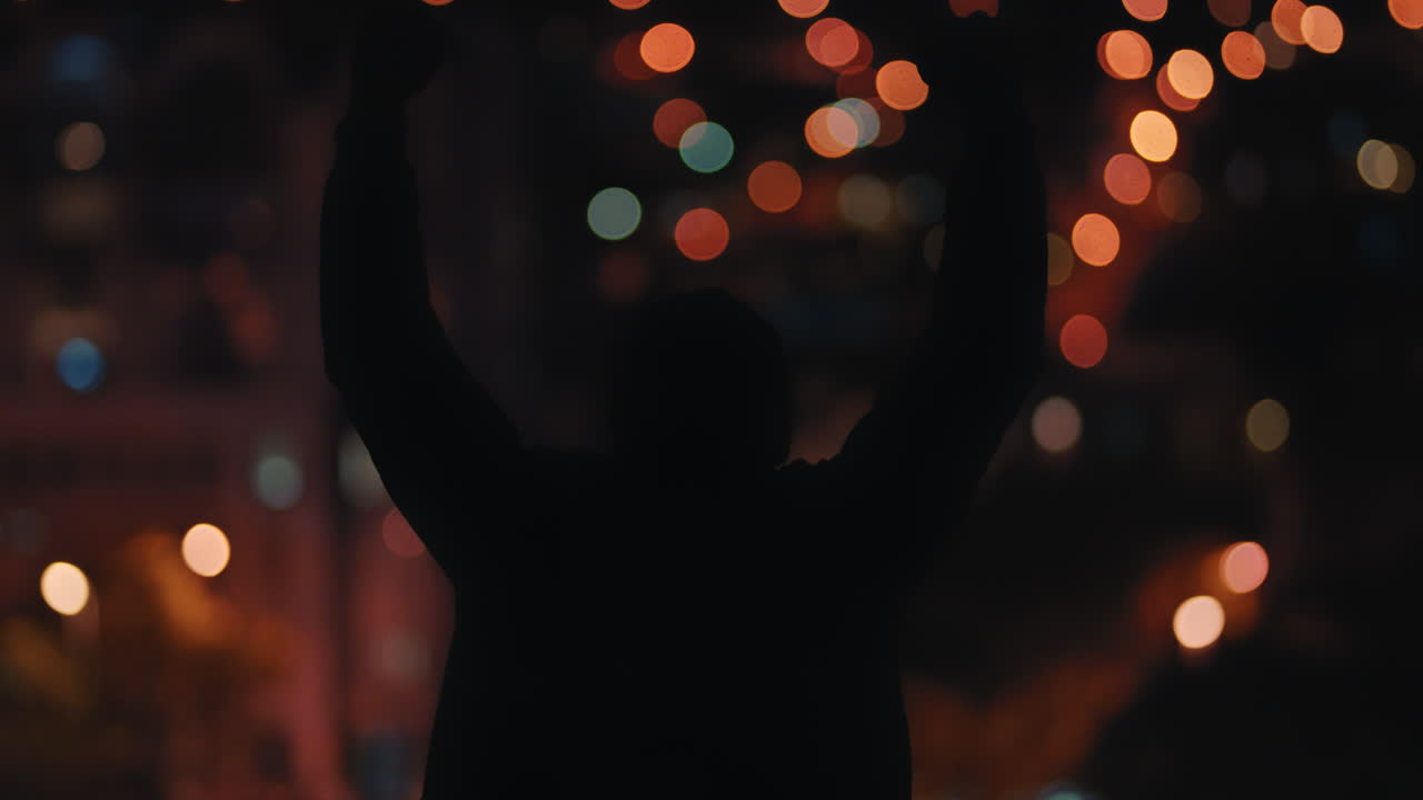 silueta de un hombre con el brazo levantado en el techo por la noche celebrando el logro de la libertad mirando las hermosas luces de la ciudad vista posterior