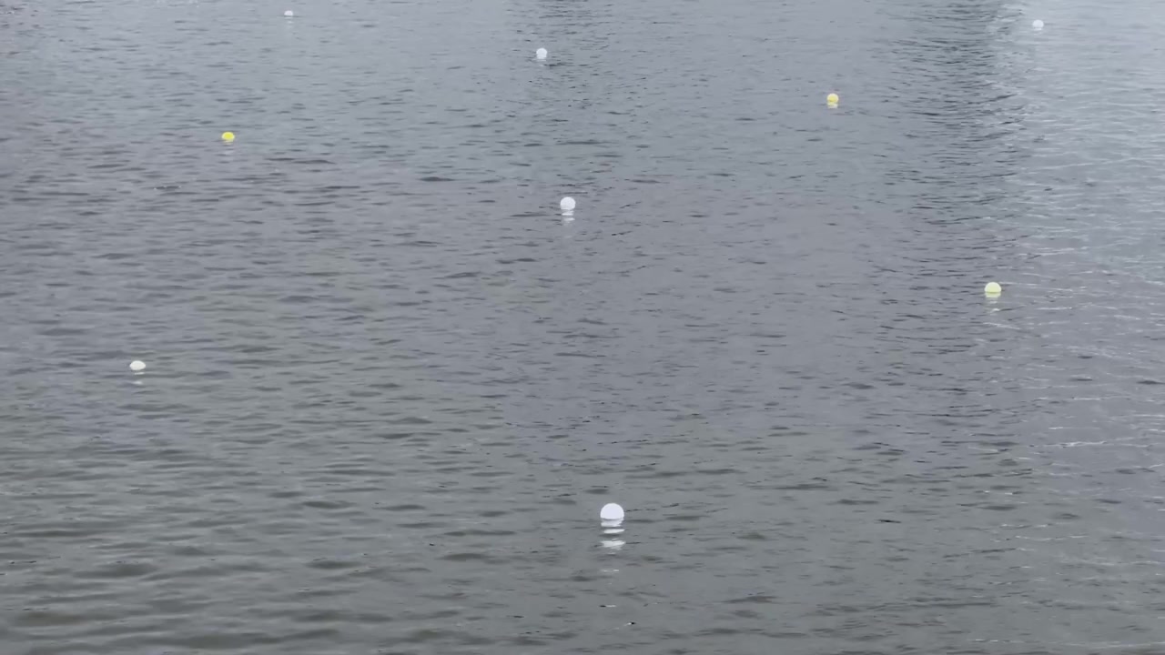 Calm lake water at a Brandenburg canoe sprint venue, showing floating lane buoys, grey ripples and minimal race course markers on an overcast day.