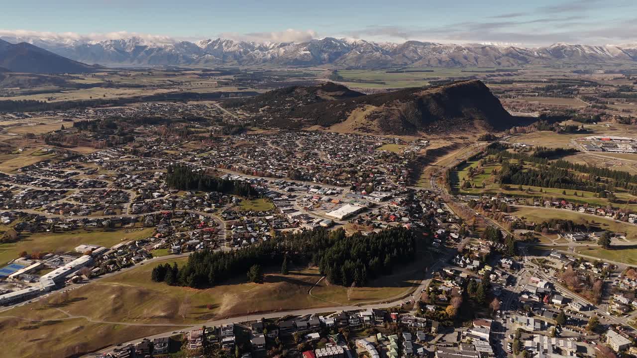A wide 4K 60fps aerial drone shot of the charming Wanaka town, nestled in the epic landscapes of New Zealand's South Island. An ideal establishing shot for content about tourism or travel