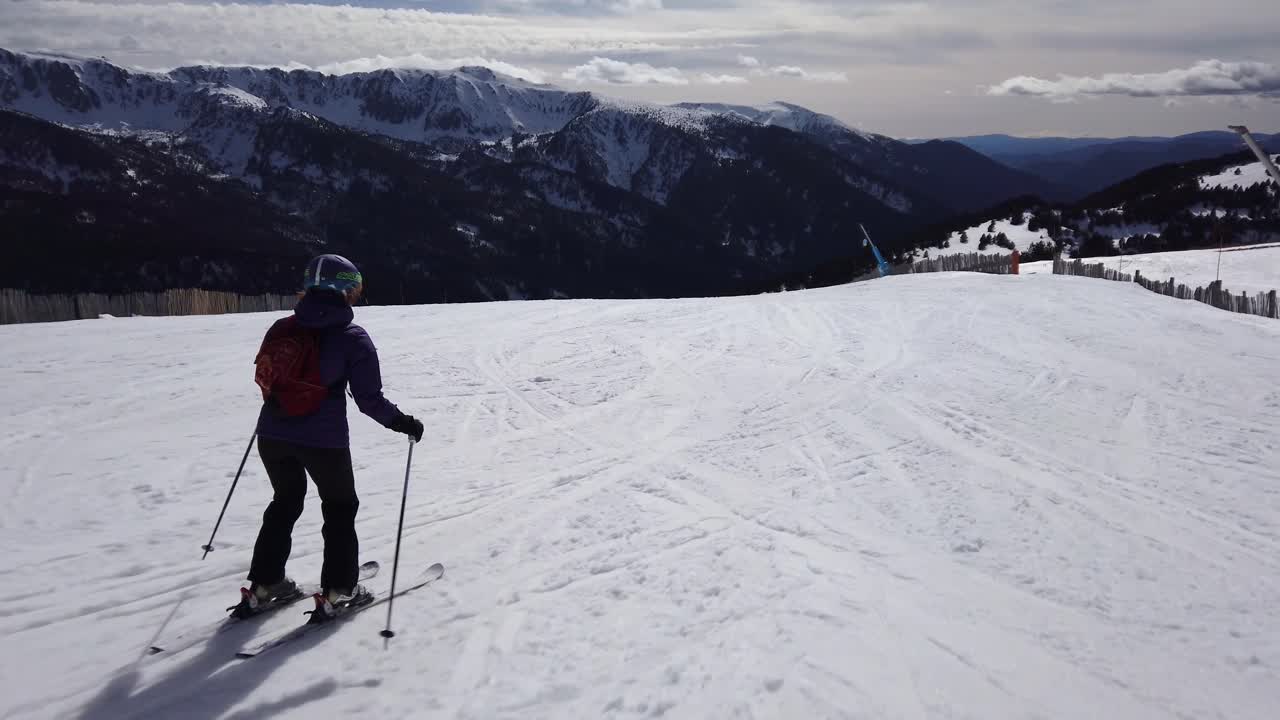 Un'inquadratura che segue una sciatrice che scende una pista in una giornata di sole.