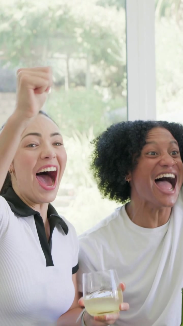 Vertical video: Score sparking group on couch at home cheering, white tee raising green beer bottle