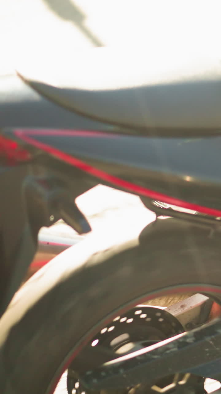 vista trasera de una motocicleta en movimiento con un primer plano de la rueda y la pierna de un jinete en zapatos de lona en el reposapiés, viaja desde un lugar soleado a un lugar sombreado