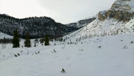 Aerial-Low-Flying-Over-Snow-Covered-Landscape-With-Forested-Hills-In-Background-In-Marebbe